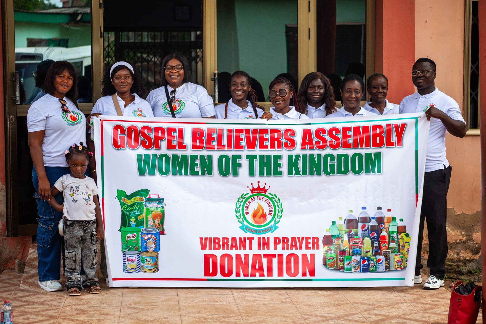 Women of the Kingdom volunteers holding a Gospel Believers Assembly donation banner at an outreach event