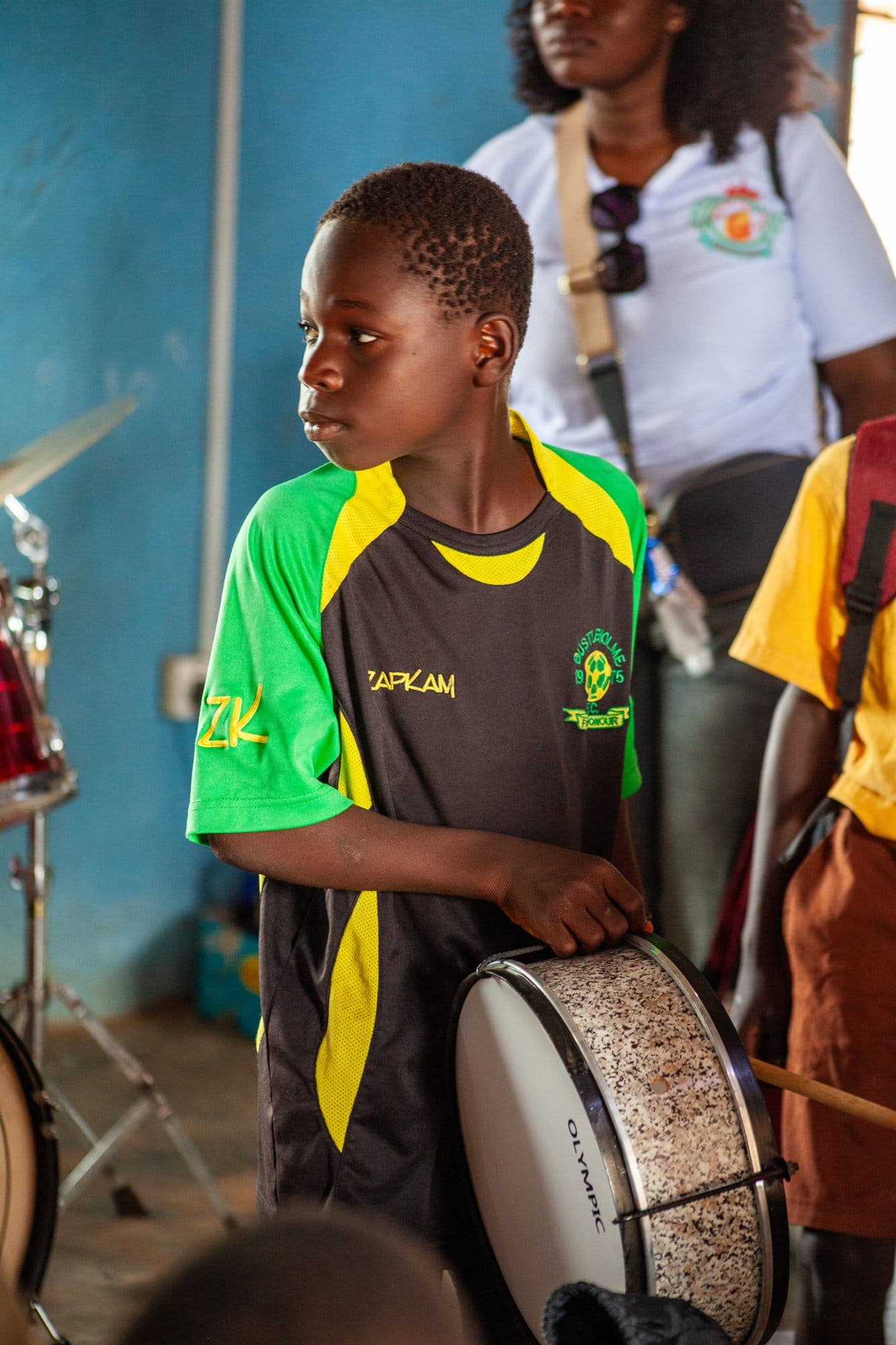A boy in a green jersey playing a donated drum at an outreach