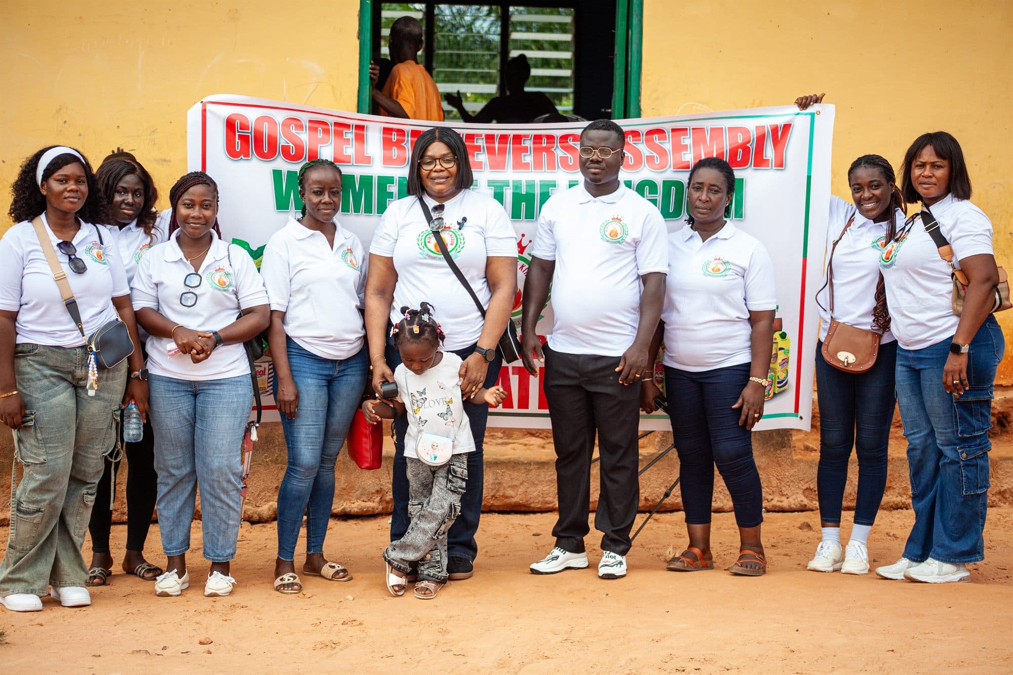Women of the Kingdom volunteers standing with a child in front of the ministry banner