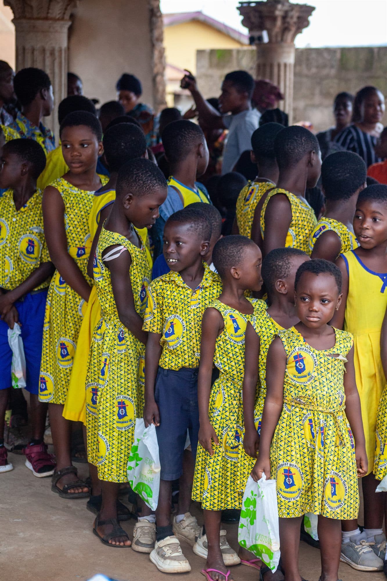 A line of schoolgirls in yellow dresses waiting at a distribution event