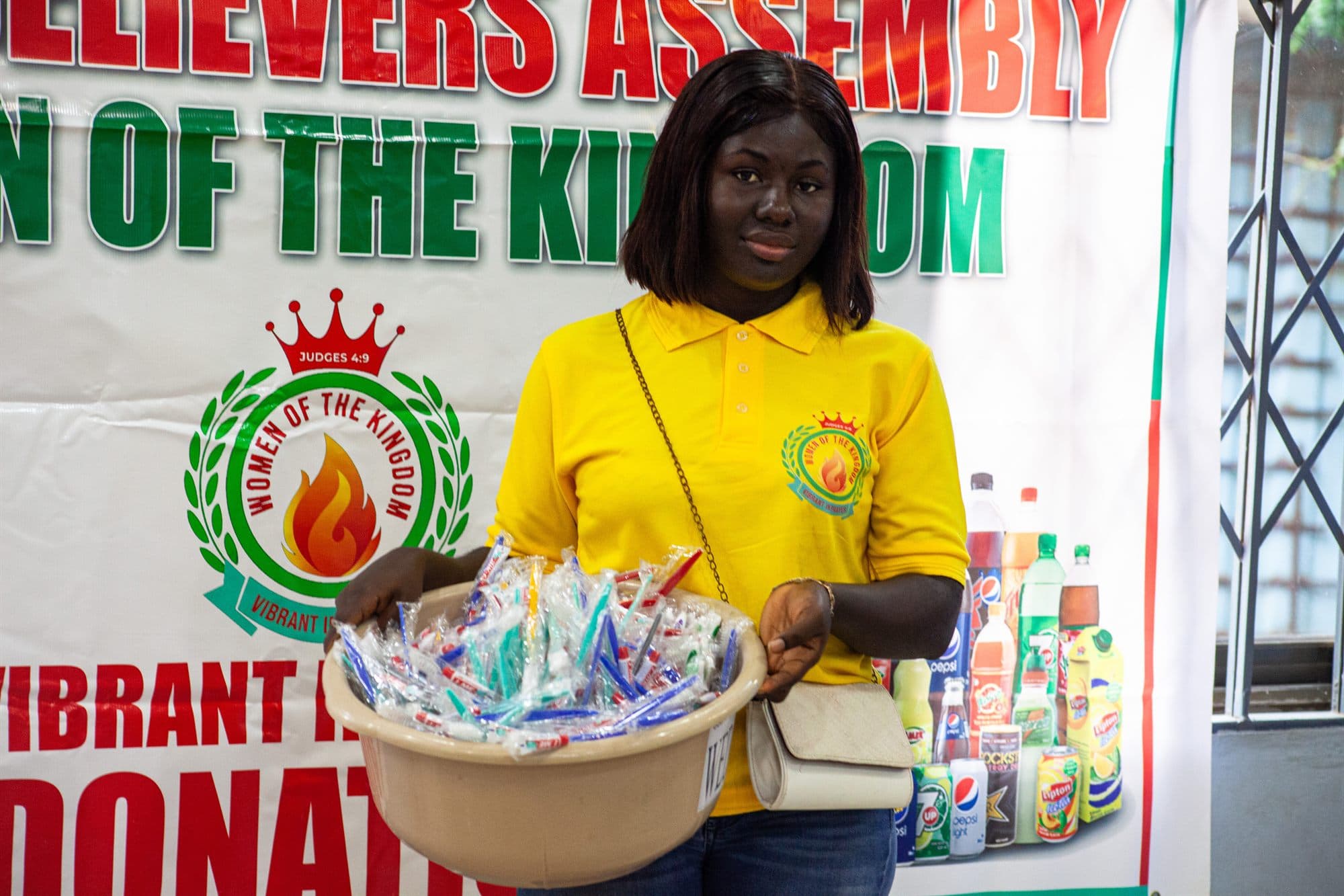 A Women of the Kingdom volunteer holding a basin of donated toothbrushes in front of the ministry banner