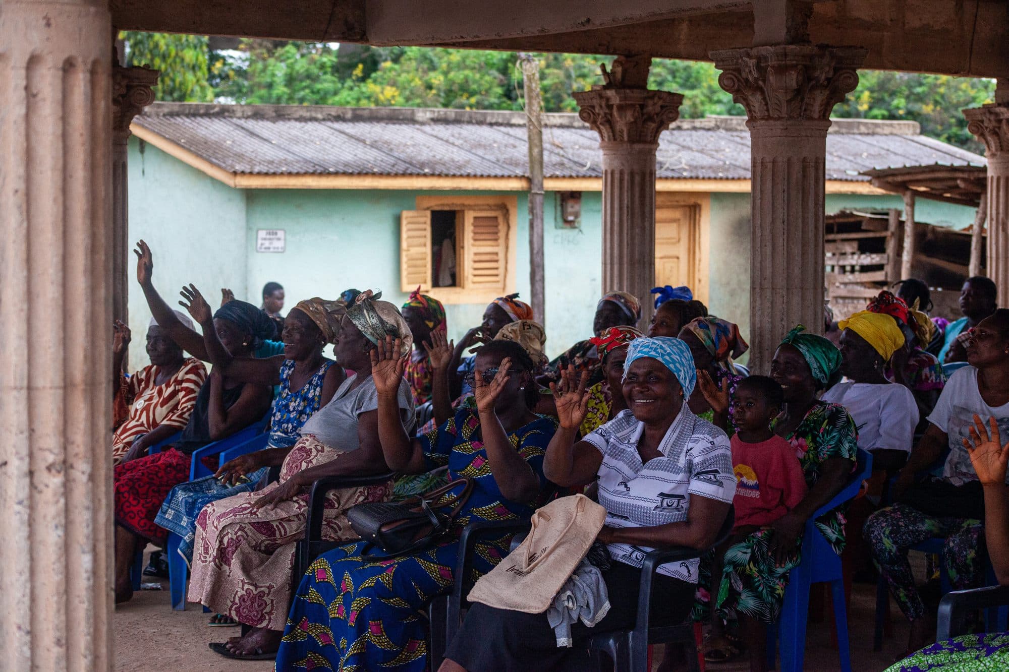 Women of the community seated together under a pavilion, waving during a Women of the Kingdom outreach gathering