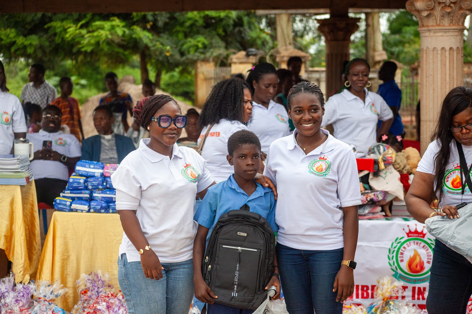Women of the Kingdom volunteers with a schoolboy holding his new backpack at a distribution day