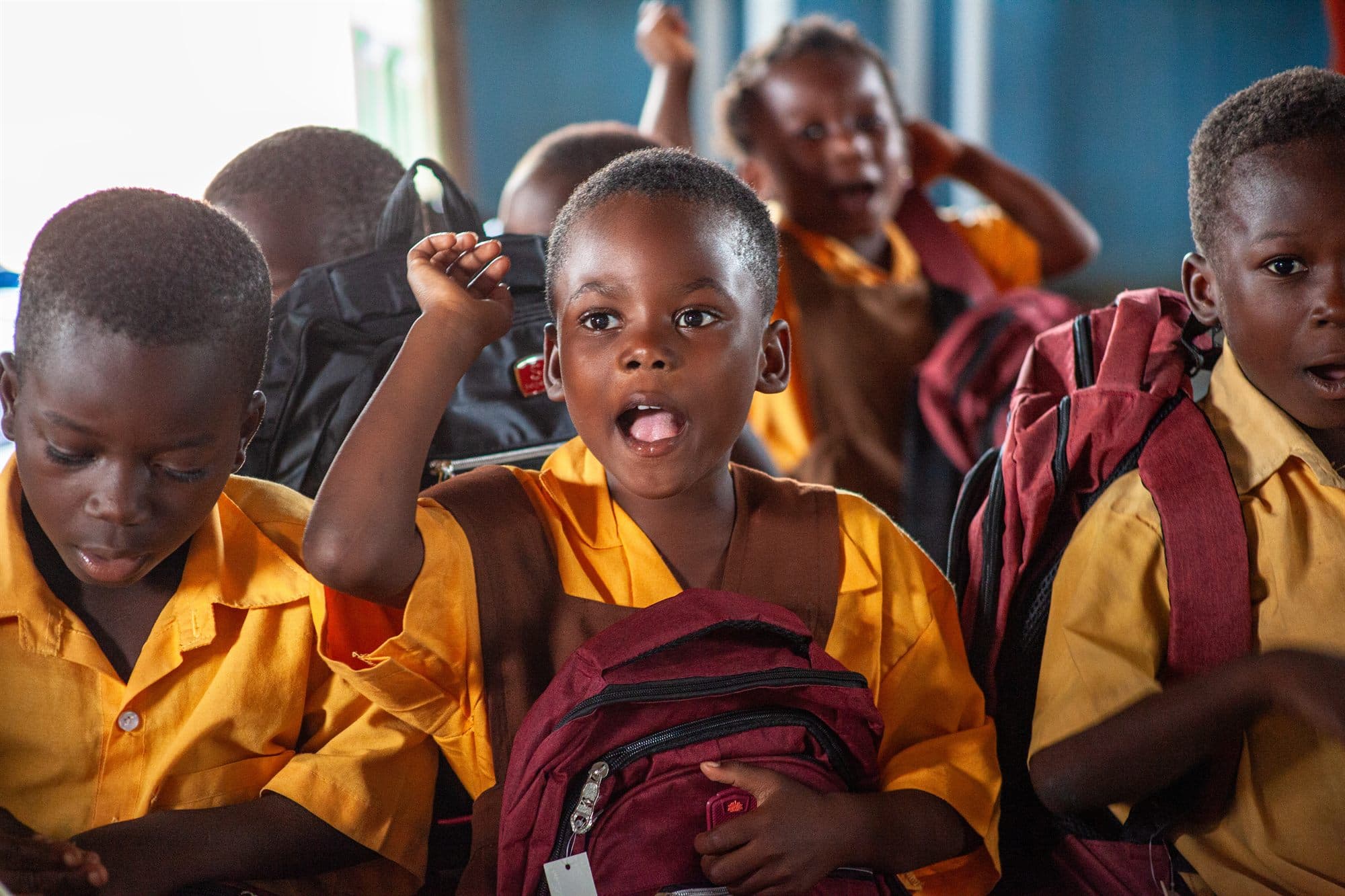 Schoolchildren in yellow uniforms with newly donated backpacks at a distribution event